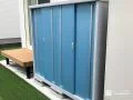 爽やかなブルーの物置が緑鮮やかな人工芝のお庭に映える工事