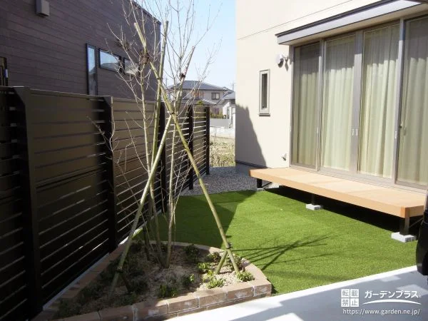 レンガで囲んだ植栽スぺースがアクセントの人工芝敷きのお庭工事